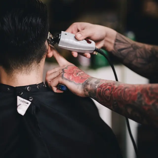 Barbero con brazos tatuados haciendo un degradado con máquina.